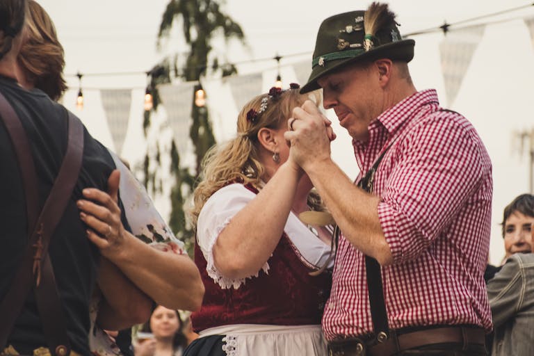 A festive couple dances at an Oktoberfest celebration outdoors, wearing traditional attire.